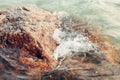 Red huge large stone rock in water on beach. Closeup of sea ocean lake wave splash with white foam. Royalty Free Stock Photo