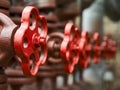 Red industrial valves in a row on petrochemical plant pipelines system selective focus over out of focus background