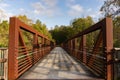 A red iron pedestrian and bicycle bridge surrounded by trees crosses over a river on the Neuse River Greenway in Raleigh, North