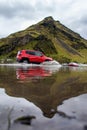 Red jeep crossing the water with a magnificent mountain in the reflection, Vik, Iceland