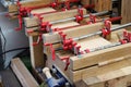 Red joiner clamps are fixed on product, gluing of boards. Bonding of wooden parts in carpentry workshop