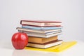 Red juicy apple lies on a yellow folder on the table, next to a stack of training books