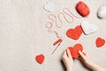 Red knit hearts for valentines day, woman hands knit work crochet heart, hook, yarn on cloth background, handcraft