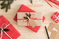 Red and kraft christmas gifts surrounded with pine cones, leaves and twine on a wooden table