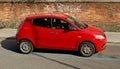 Red Lancia Ypsilon, city car of Fiat Group, on brick wall background.