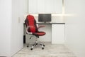 Red leather comfortable chair on wheels stands in a white room with monitor, white cabinet interior Royalty Free Stock Photo