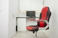 Red leather comfortable chair on wheels stands in a white room with a table and a monitor Royalty Free Stock Photo