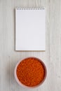 Red lentils in a pink bowl, blank notepad on a white wooden surface, top view. Flat lay, overhead, from above. Space for text Royalty Free Stock Photo