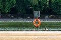 Red life float under a sign on the shore of a green pond