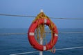 Red lifebuoy on rope handrails at the sea dock. The rescue rope is wrapped around the pole in disarray