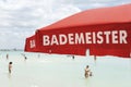 Red lifeguard umbrella on a beach against blue sky. Some bathers ont he background. The text on the umbrella Bademeister Royalty Free Stock Photo