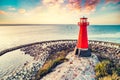 Red lighthouse on rocky harbor at sunset Royalty Free Stock Photo