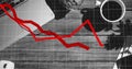 Red line graph displaying decline, covering a desk with a laptop and coffee
