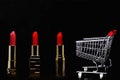 Red lipstick, gold bars and shopping cart isolated on black background with copy space