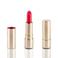 Red lipstick in golden tube on white background with mirror reflection on glass surface isolated close up, shiny gold lipsticks