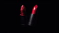 a red lipstick is next to a black lipstick tube on a black background with a red glittered surface on the tip of the lipstick