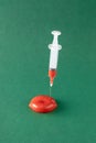 The red liquid in the medical syringe is injected into the red lips. Minimal concept on a dark green background. A symbol of