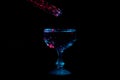 Clear liquid lit in red lights falling into a glass chalice like a meteor lit in blue and red isolated on a black background