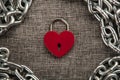 Red locked heart shaped padlock with steel chain on gray linen textile