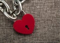 Red locked heart shaped padlock with steel chain on gray linen textile