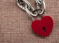 Red locked heart shaped padlock with steel chain on a linen textile