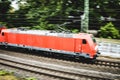 Red locomotive speeding through a green lush forest with the cables above