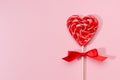 Red lollipop heart with silk bow on pastel pink as festive valentine`s day background.