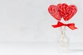 Red lollipops hearts with silk bow in glass vase in white interior as festive valentines day background.