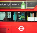 Red London bus with a lone female passenger in face mask sitting.