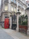 Red London telephone box by nice black gates and blooming tress