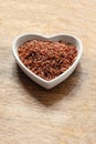 Red long grains rice in heart shaped plate on wooden background close up