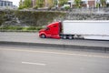 Red long haul big rig semi truck with broken fender transporting cargo in dry van semi trailer running on the city highway