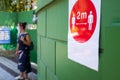 Red 2m social distance sign on green wall on the street with woman in background Royalty Free Stock Photo