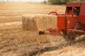 Red machine forms straw bales, agricultural work, yellow straw bale close up, agriculture