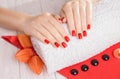 Red manicure with dekor and towel on white wooden table.