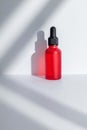 Red matte glass cosmetic dropper bottle with blank label on white background with gobo shadows. Trendy beauty product Royalty Free Stock Photo