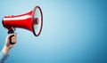 A red megaphone held by a hand against a blue background with copy space Royalty Free Stock Photo