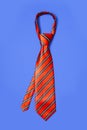 Red men`s striped tie taken off for leisure time, isolated on blue Royalty Free Stock Photo