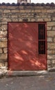 Red metal door with lattice closed on chain with lock in old stone wall. Vertical photo Royalty Free Stock Photo