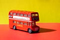 A red miniature toy bus, London Route Master bus. against a bright red and yellow background with black shadows Royalty Free Stock Photo
