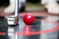 Red minigolf ball and an iron racket at a minigolf court