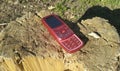 Red mobile phone 2000s rests on a wooden stump