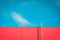 A red modern facade of an industrial building, warehouse or shopping center with a long metal staircase against the blue sky. Royalty Free Stock Photo