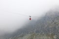 Red mountain cableway car in clouds and fog