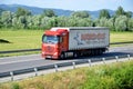 Red moving Mercedes-Benz Actros truck coupled with semi-trailer located on slovak D1 highway surrounded by green field and trees. Royalty Free Stock Photo