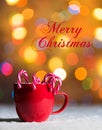 Red mug with candy canes in snow with defocussed fairy lights, bokeh in the background, Festive Christmas background Royalty Free Stock Photo