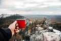 a red mug with coffee or tea in the hand of a man in the mountains Royalty Free Stock Photo