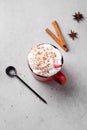 Red mug with hot chocolate or cocoa with whipped cream, spoon, cinnamon sticks and star anise scattered on a blue background.