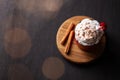 Red mug with hot chocolate or cocoa with whipped cream on a wooden stand with cinnamon sticks on a dark background with a garland