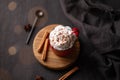Red mug with hot chocolate or cocoa with whipped cream on a wooden stand with cinnamon sticks and star anise scattered around on a
